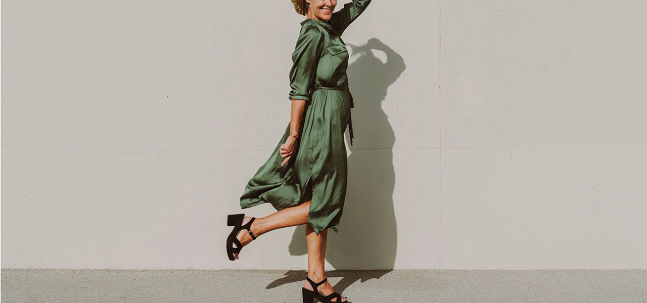 smiling woman in green dress stands on one foot.