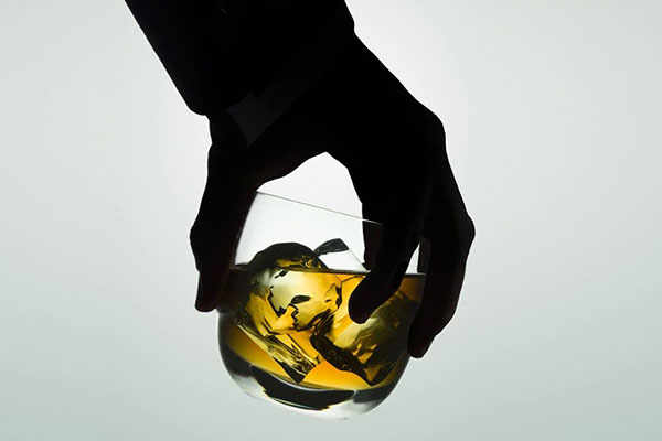 hand in shadow holding glass of liquor