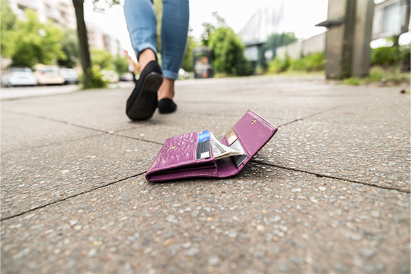 A woman losing her wallet on the sidewalk. 