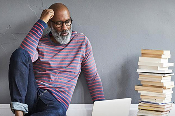Person using a laptop next to a stack of books.