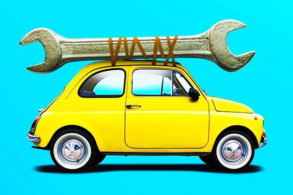 Small yellow car with a large wrench strapped to its roof.