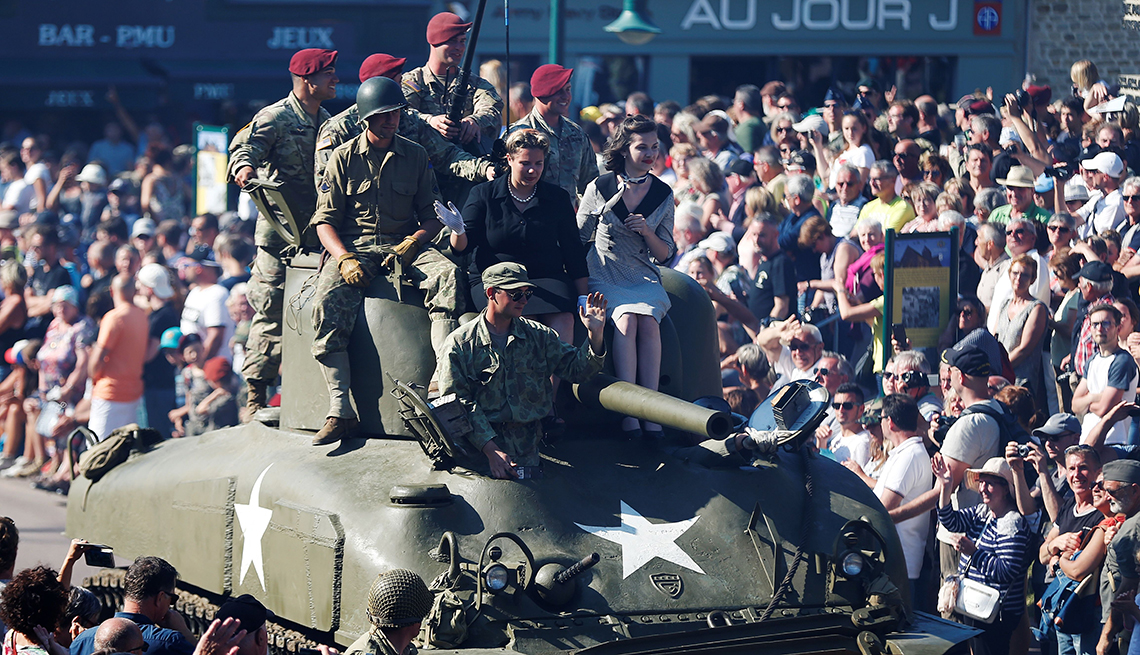 Entusiastas de la Segunda Guerra Mundial están sentados en un tanque de guerra durante un desfile en Sainte-Mere-Eglise, en el noroeste de Francia, el 3 de junio de 2018.