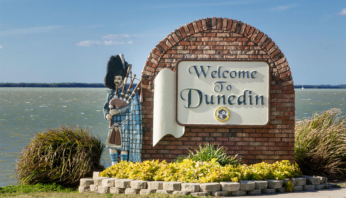 statue of man with bag pipes standing next to the Welcome to Dunedin sign 