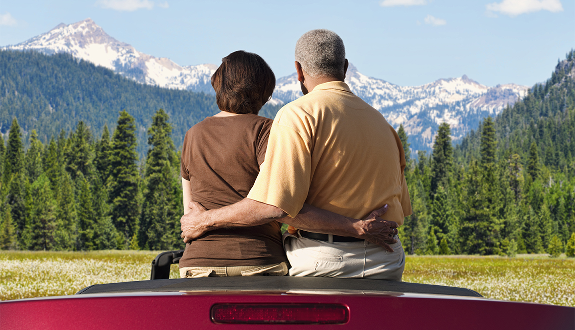 Pareja sentada en un auto convertible mientras observan árboles y montañas