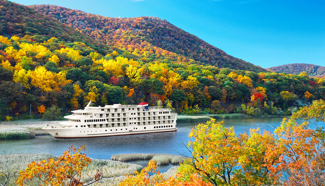 cruise ship sailing on a large river surrounded by hills of fall foliage