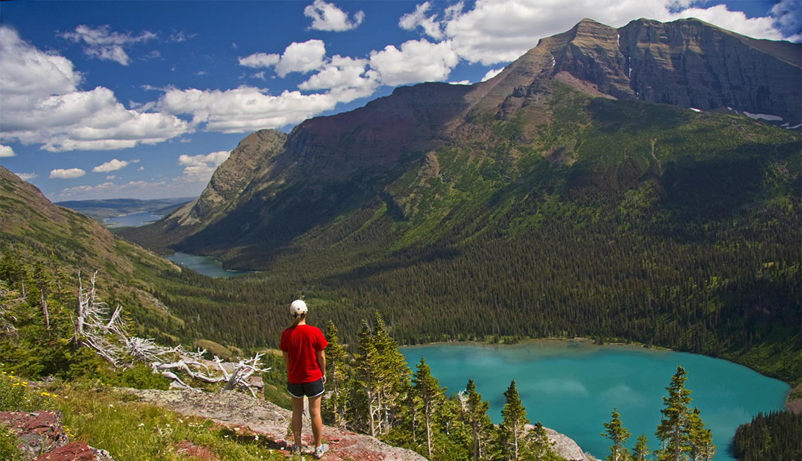 Young woman in red overlooking Grinnell Lake on the Grinnell Glacier Trail in Glacier National Park