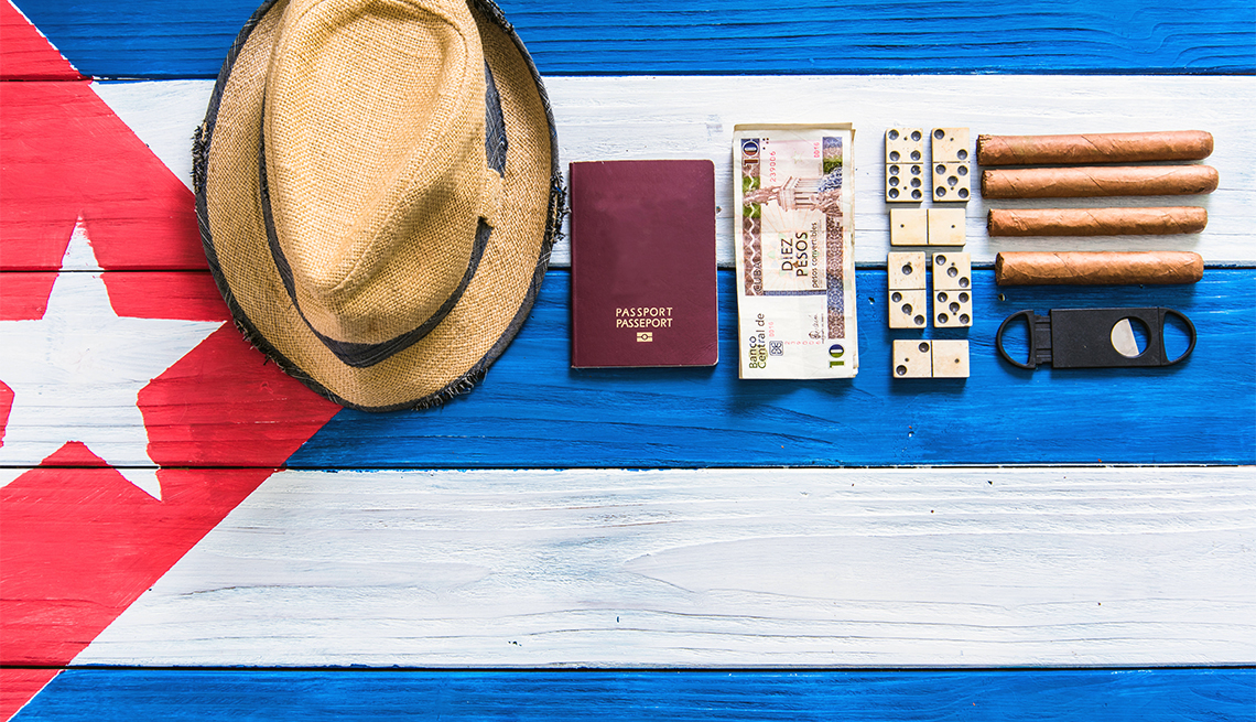5 maneras de ir a Cuba - Sombrero, pasaporte, tabacos y dinero, sobre una bandera cubana