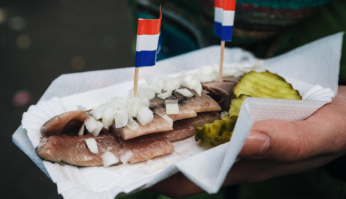 Una mano sostiene una comida tradicional holandesa con pepinillos y cebollas.