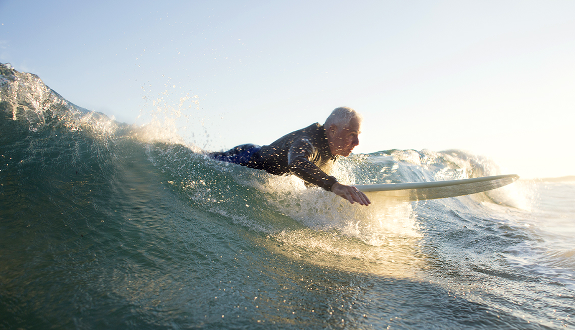 Older man in wetsuit surfing a wave at sunset