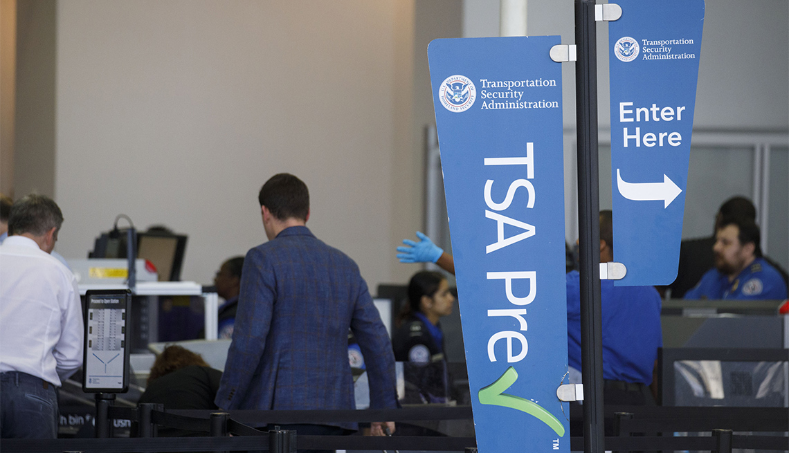 A Transportation Security Administration (TSA) PreCheck sign is displayed as travelers carry baggage through a security checkpoint