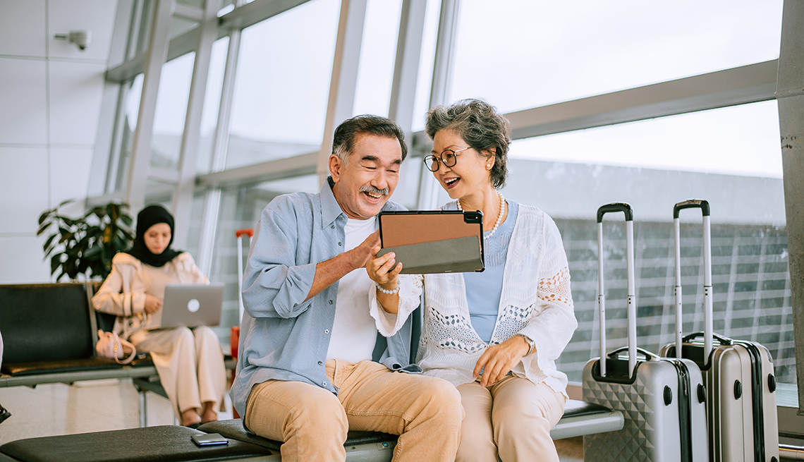 Una pareja ven una tableta mientras esperan sentados en el aeropuerto.