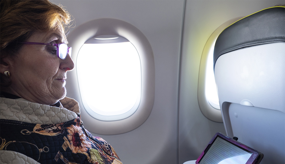 Mujer mayor sentada al interior de un avión observa su tableta electrónica