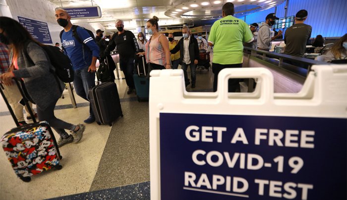 Viajeros pasan por delante de un letrero que les indica que obtengan una prueba rápida COVID-19 gratis