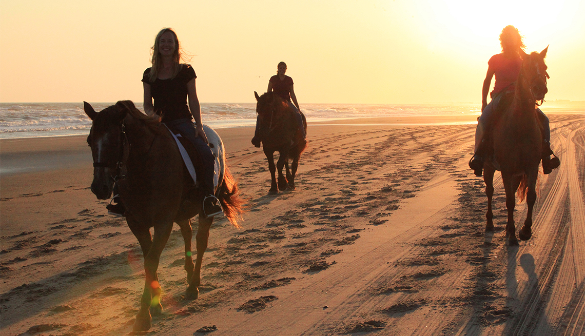 Tres personas montan a caballo en la playa