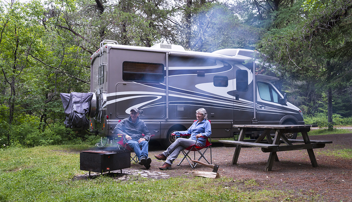 Couple relaxing near campfire with an RV in the background