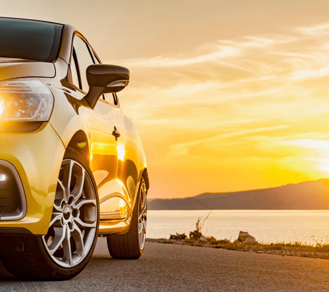 close up of a gold car parked near the water during sunset