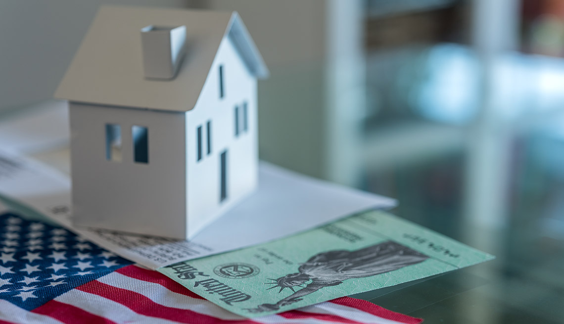a model display of a home on top of an IRS envelope, U.S. stimulus check and American flag 
