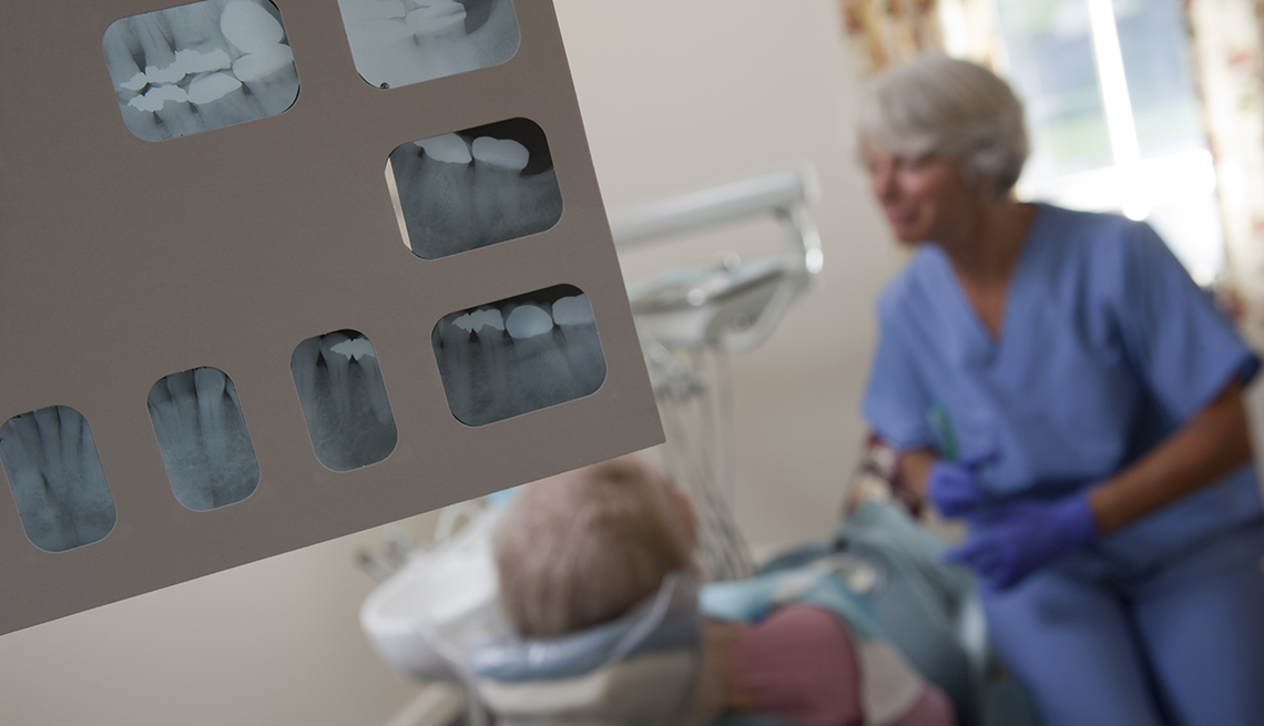 An X-Ray of a patient's dental work is shown in a room where a dental hygienist works with a patient