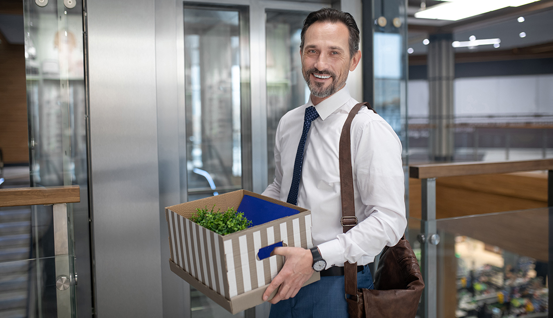 Hombre sosteniendo una caja con objetos personales cerca al elevador de una oficina.
