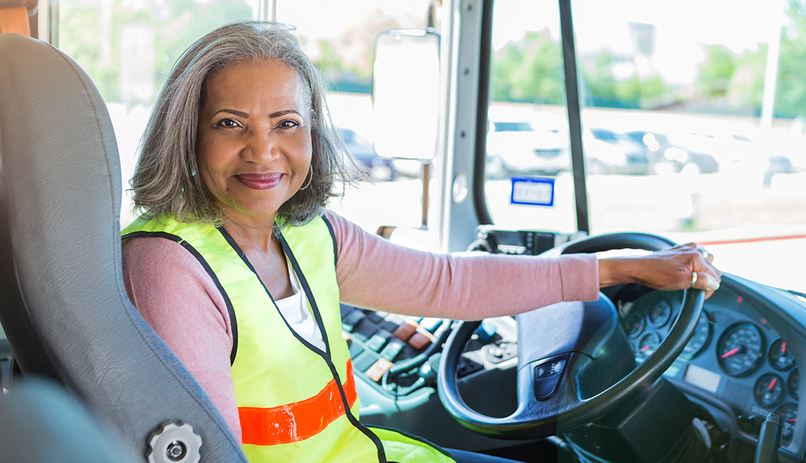 smiling senior female bus driver turns to look at the camera from the driver's seat of her school bus