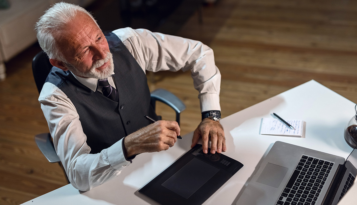 Hombre mayor sentado frente a un escritorio y viendo su computadora.