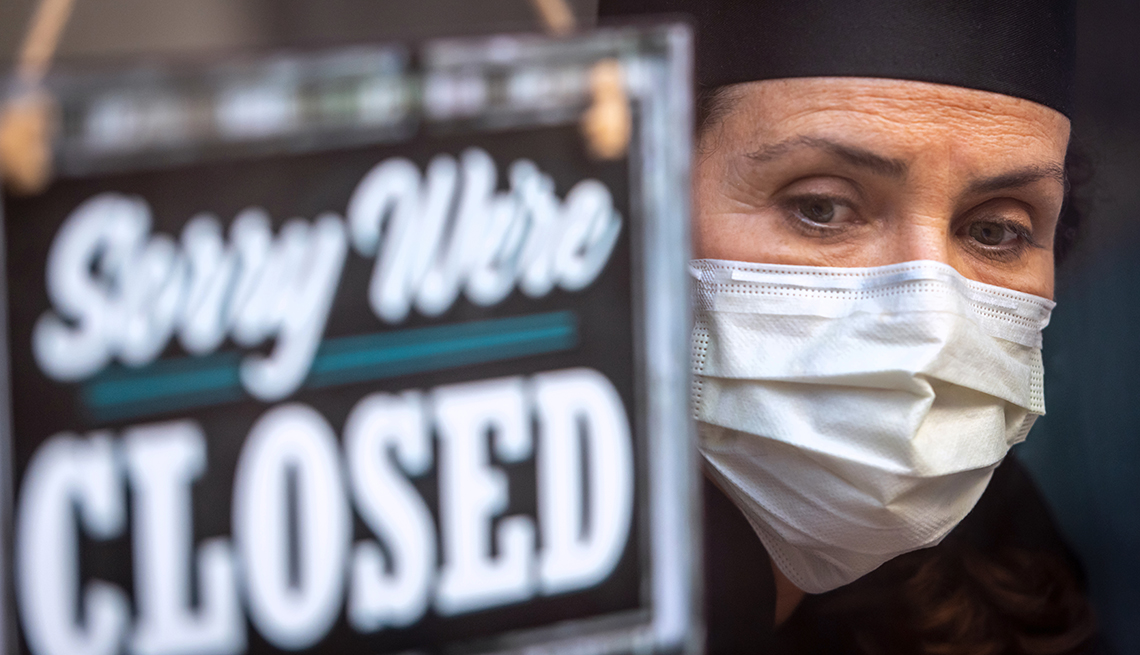 A woman in a mask stands next to a sign that says sorry we're closed