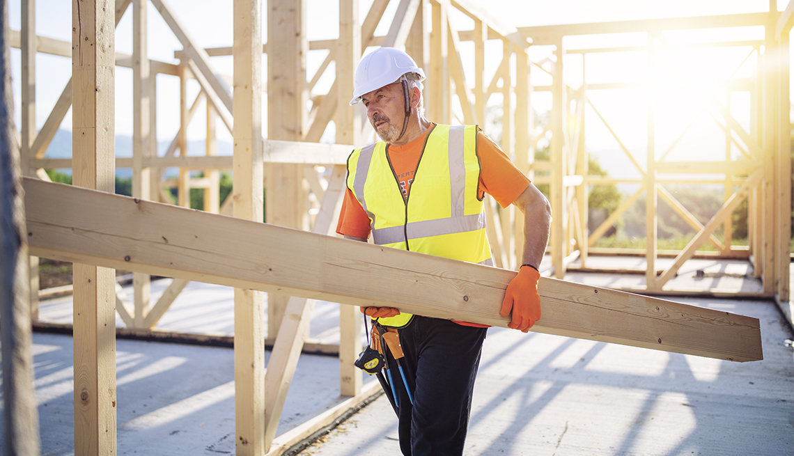 Trabajador de la construcción lleva una viga de madera en una obra