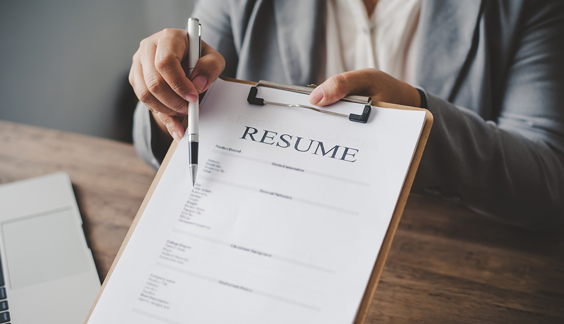 person holding a resume on a clipboard pointing to a section