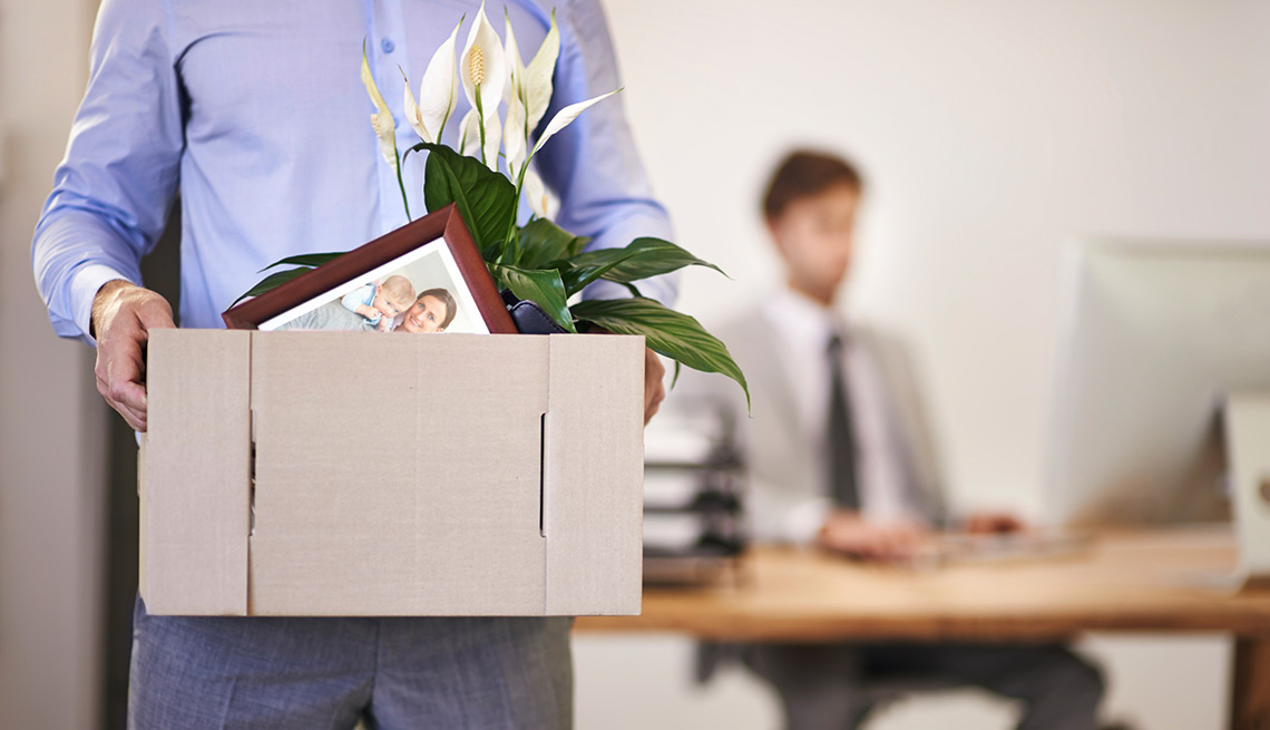 Hombre con una caja llena de objetos personales en las manos mientras camina en una oficina - Errores que afectan tus beneficios de desempleo