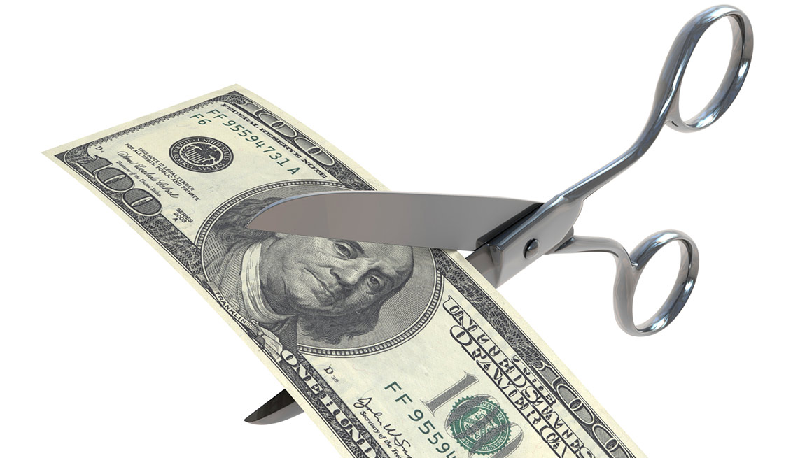 Un billete de 100 dólares y unas tijeras a punto de cortarlo - Considerar el recorte de salario