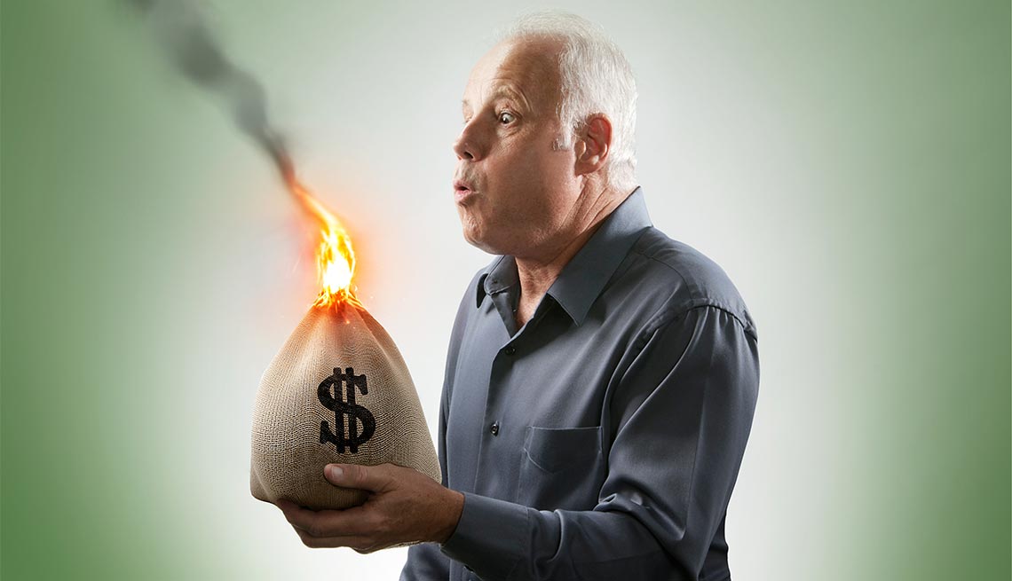 Un hombre sopla una llama de fuego que sale de una bolsa de dinero que sostiene en sus manos