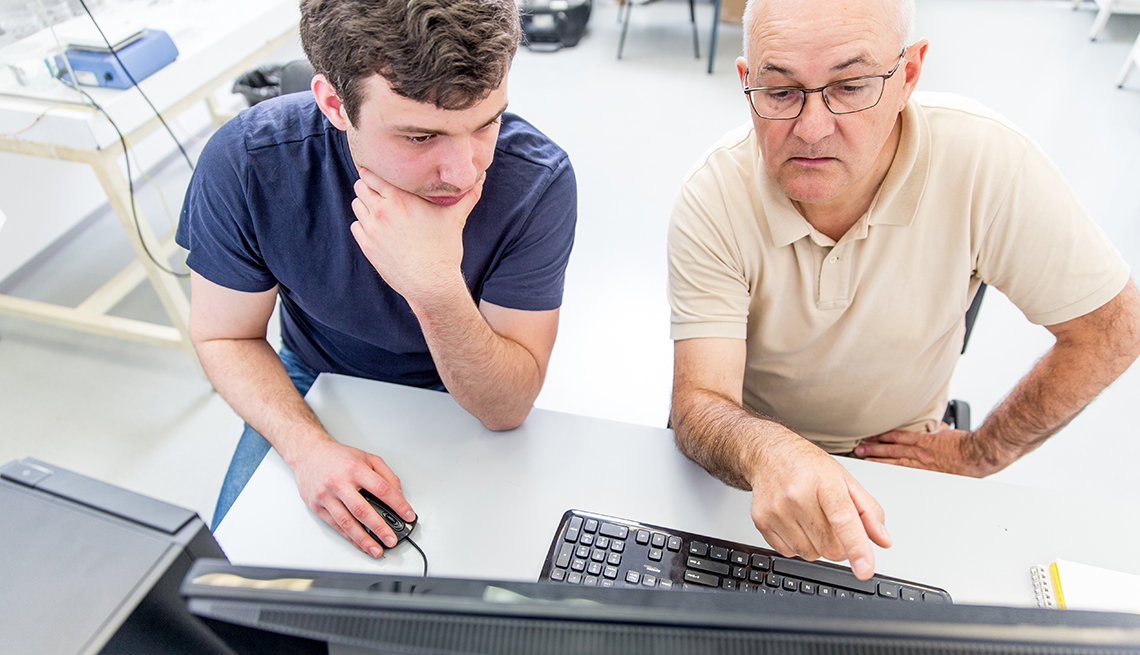 Hombre joven al lado de uno mayor quien es su mentor viendo una computadora.