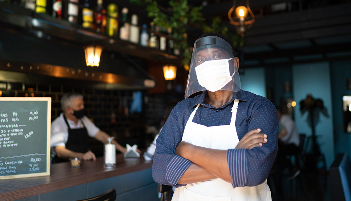 Trabajador de un restaurante usando mascarilla y pantalla facial con los brazos cruzados.