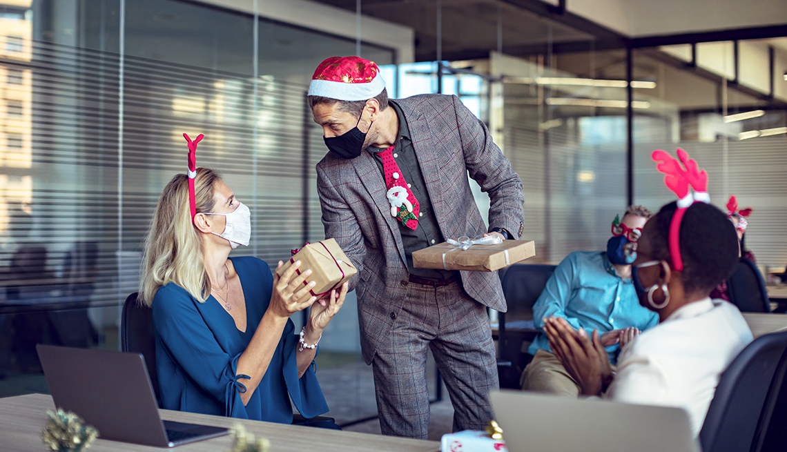 Empleados en una oficina en una fiesta de navidad con gorros navideños y mascarillas