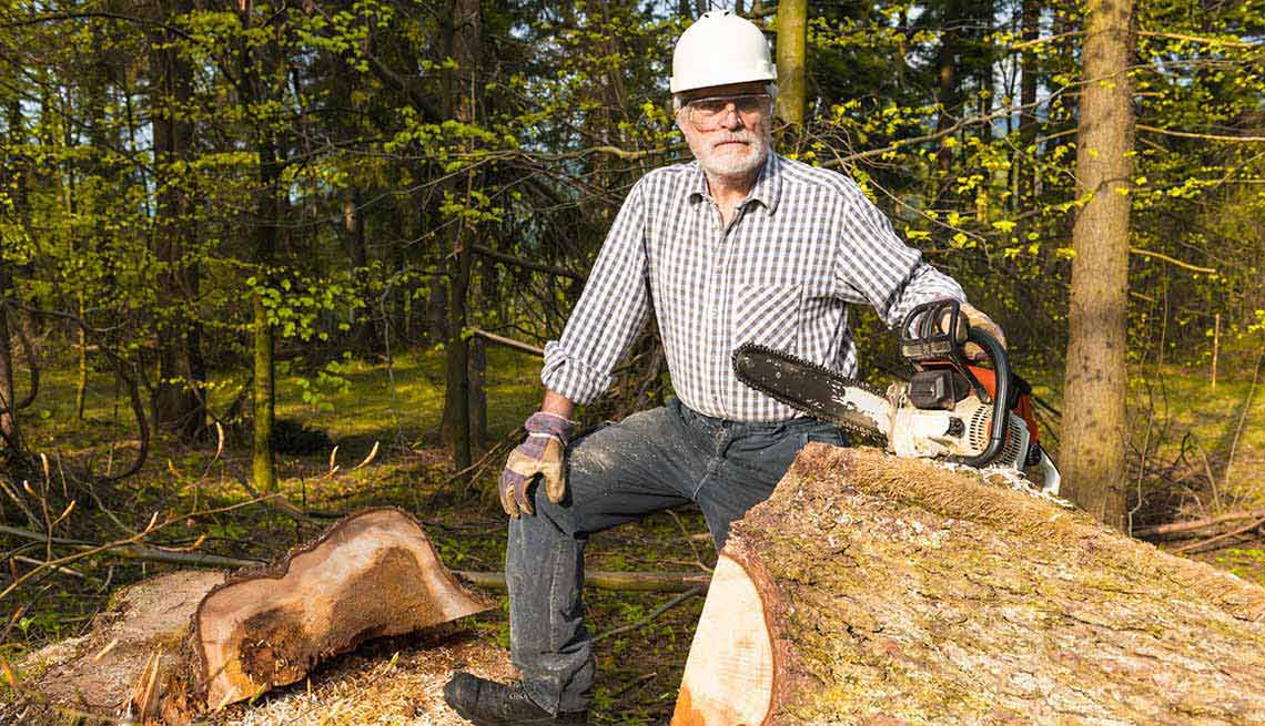 Hombre con una sierra eléctrica al lado de un tronco de árbol
