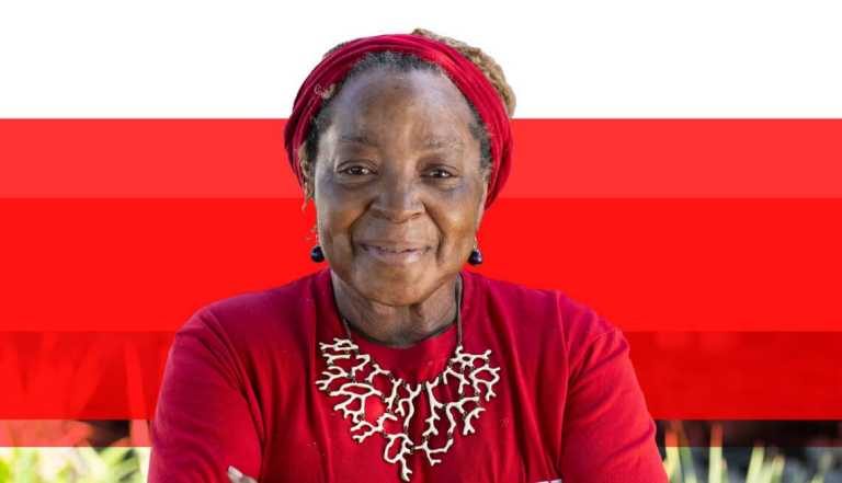 African American senior woman smiling wearing red shirt , head band, and necklace against a red background