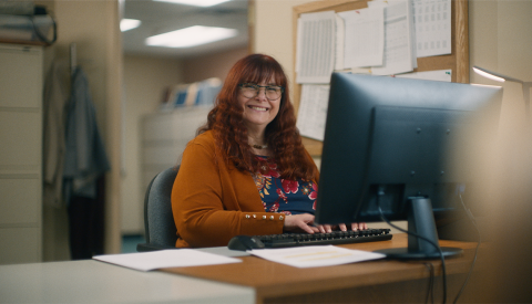 A smiling middle aged woman sitting at a desk and typing on her computer