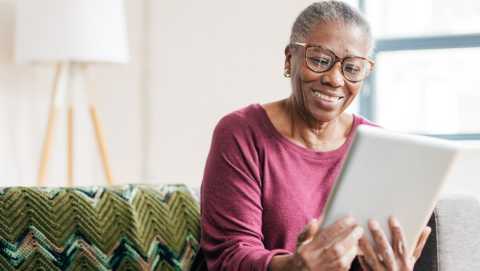 Older woman of color smiling and looking at her tablet. 