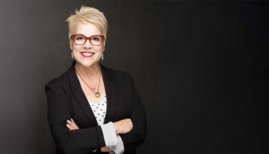 Photo of Kat Willis wearing red glasses, black blazer, white and black polka dot shirt, and gold necklace with arms crossed, BACK TO WORK50+ program participant