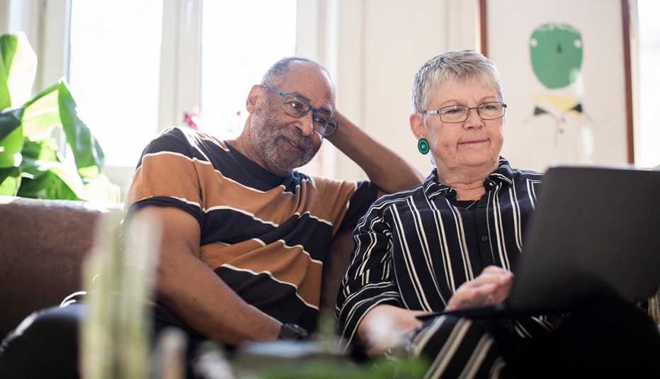 Two older adults review paperwork together at a laptop. 