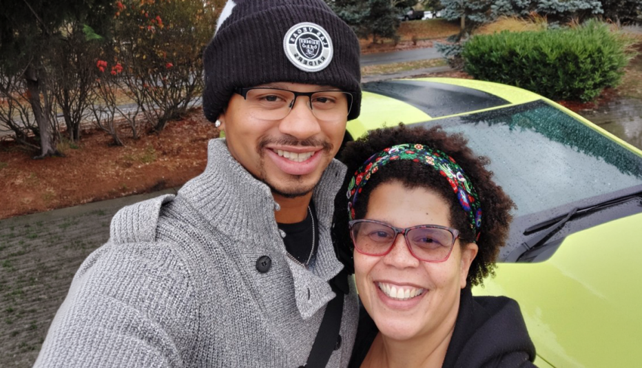 Older woman standing next to her taller son in front of a yellow car outside