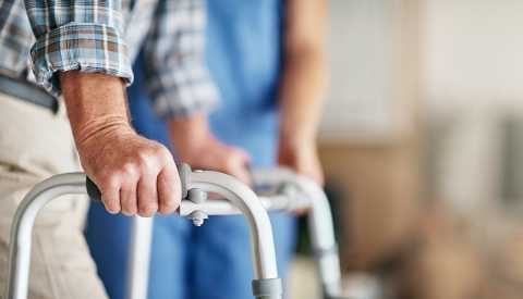 Shot of a woman assisting her elderly patient who's using a walker for support.