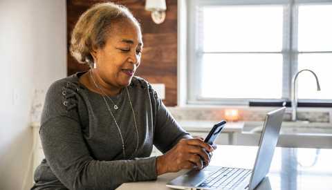 Senior woman working using laptop in residential kitchen.