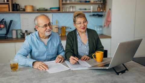 Senior man and woman looking at financial document and bills, using the internet to pay mortgage loans.