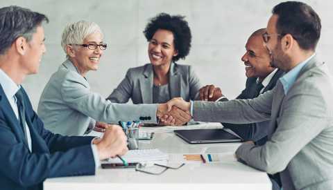 Older businesswoman and businessman shaking hands across the table 