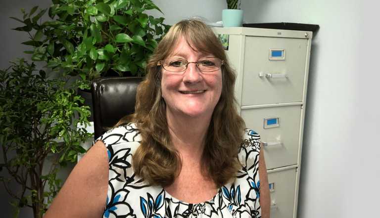 woman wearing glasses and sitting in a chair with plants and a file cabinet behind her