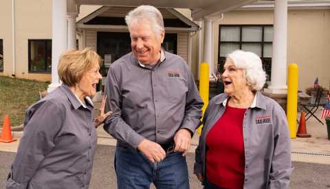 Sisters Charlotte (left) and Carolyn flank Carolyn’s husband, Jeff – outside the senior center where all three volunteer for Tax-Aide.