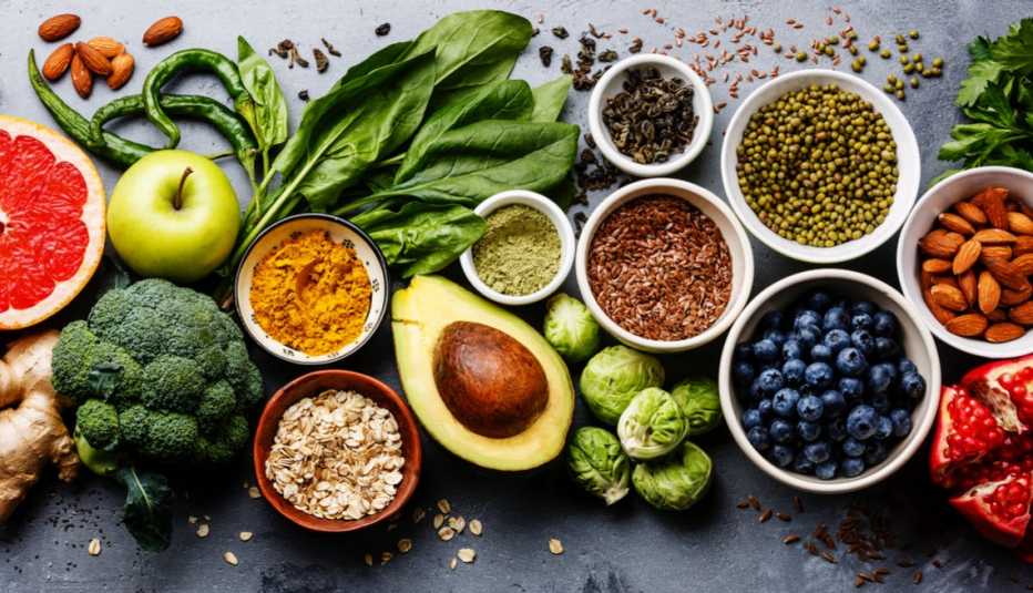 Assortment of healthy foods including broccoli, apple, avocado, nuts, seeds, greens, blueberries