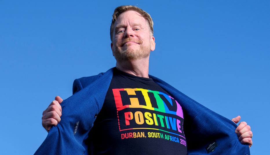 mark king revealing a shirt that says h i v positive