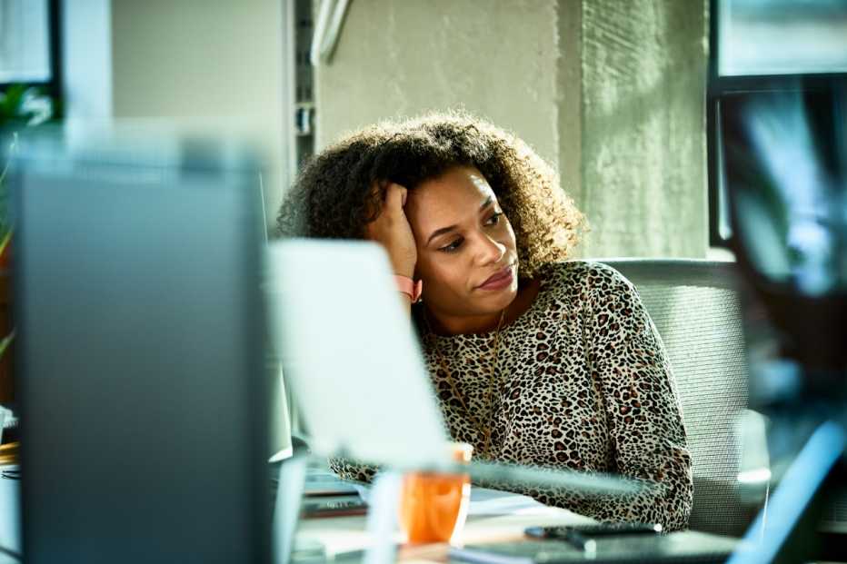 Close up view of mid adult businesswoman in animal print blouse, resting head on hand in office, introspection, daydreaming, distraction, pensive